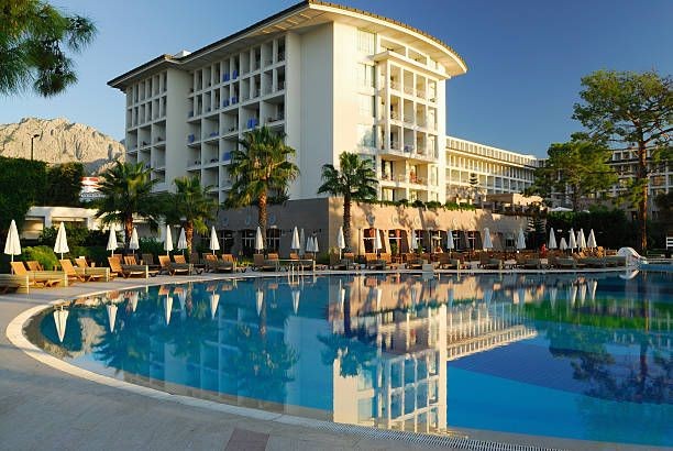 Luxury hotel with palm trees and a large outdoor swimming pool reflecting the building at sunset.